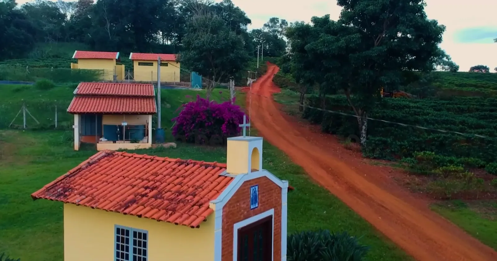 A capela do sítio ao lado da estrada de terra, com as casas de apoio e a lavoura ao fundo